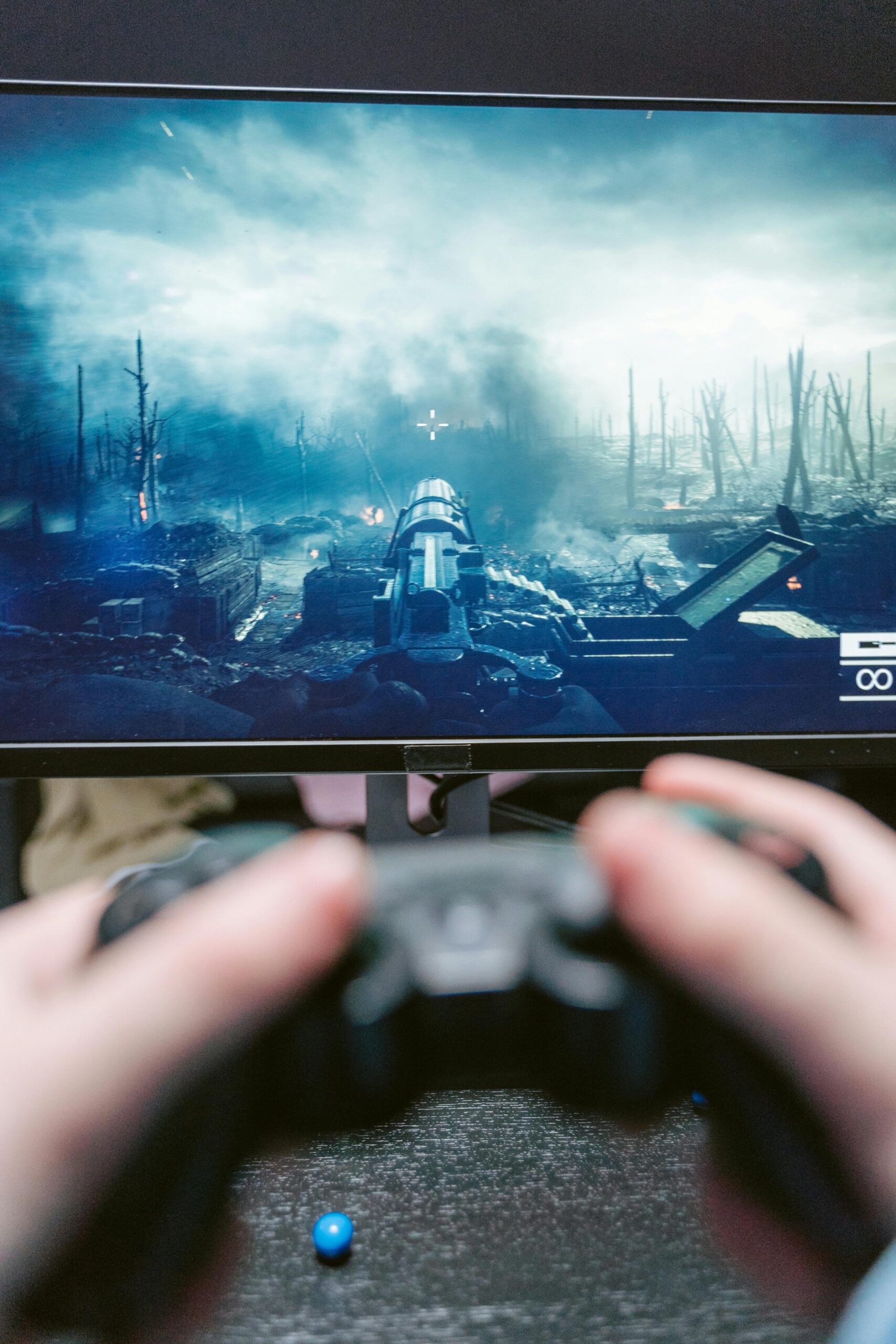 Hands gripping a game controller with action displayed on a monitor in the background.